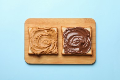 Photo of Delicious sandwiches with peanut butter and chocolate paste on light blue table, top view