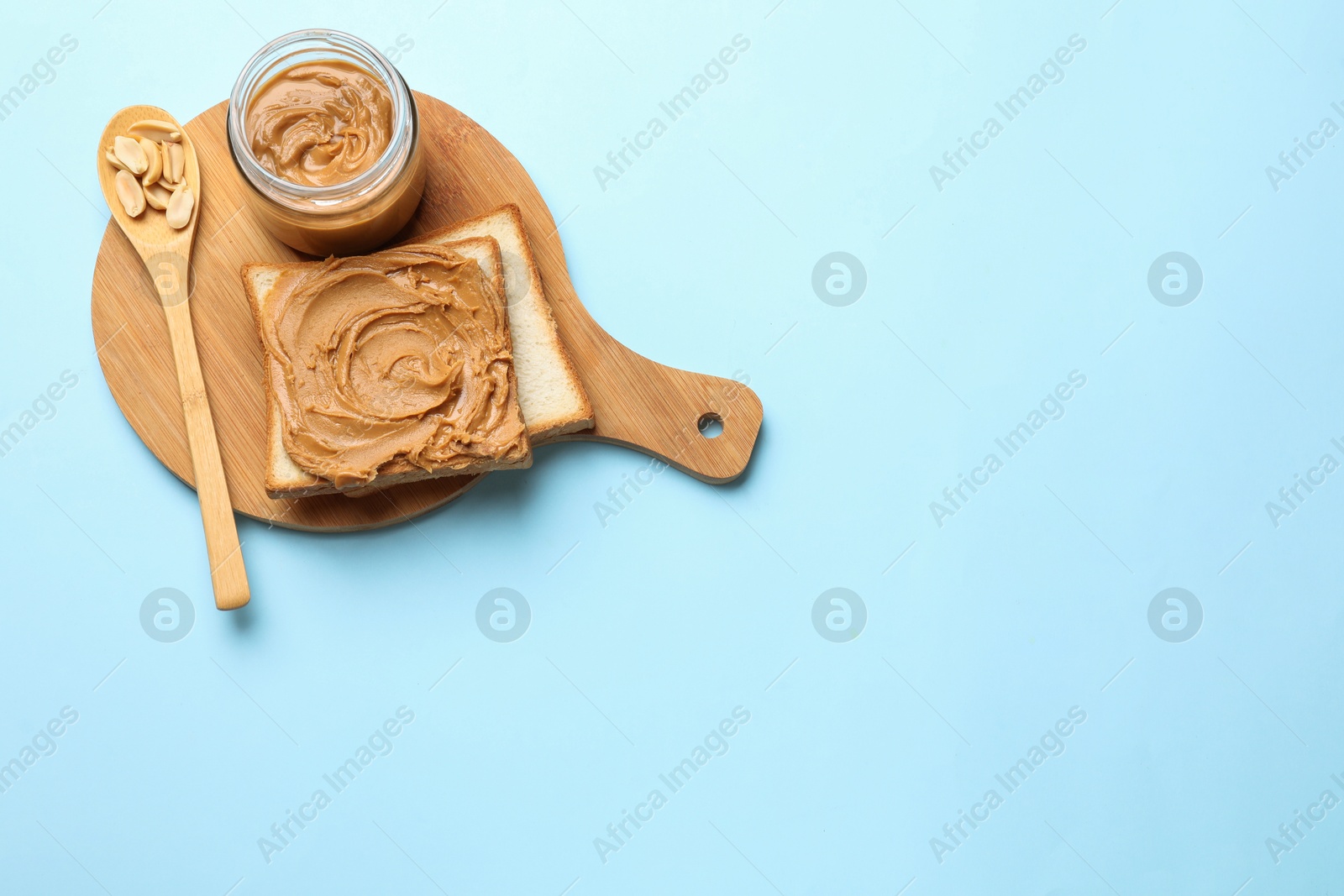 Photo of Delicious sandwich with peanut butter and fresh nuts on light blue table, top view. Space for text