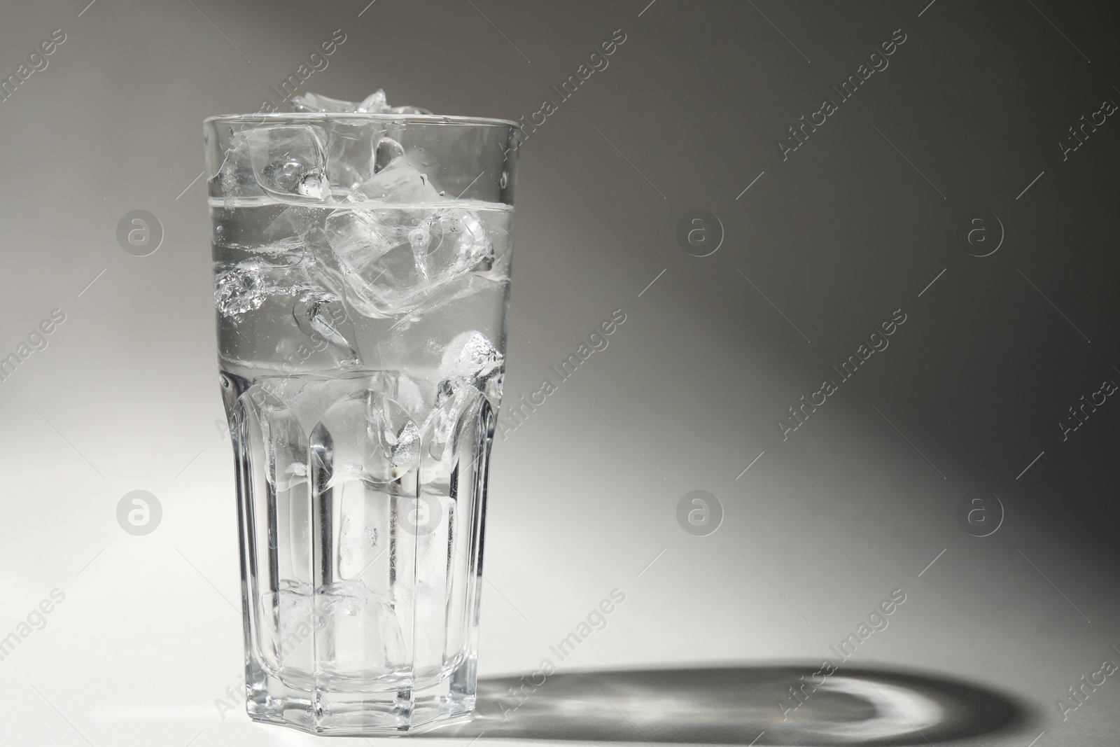 Photo of Refreshing water with ice in glass on grey background. Space for text