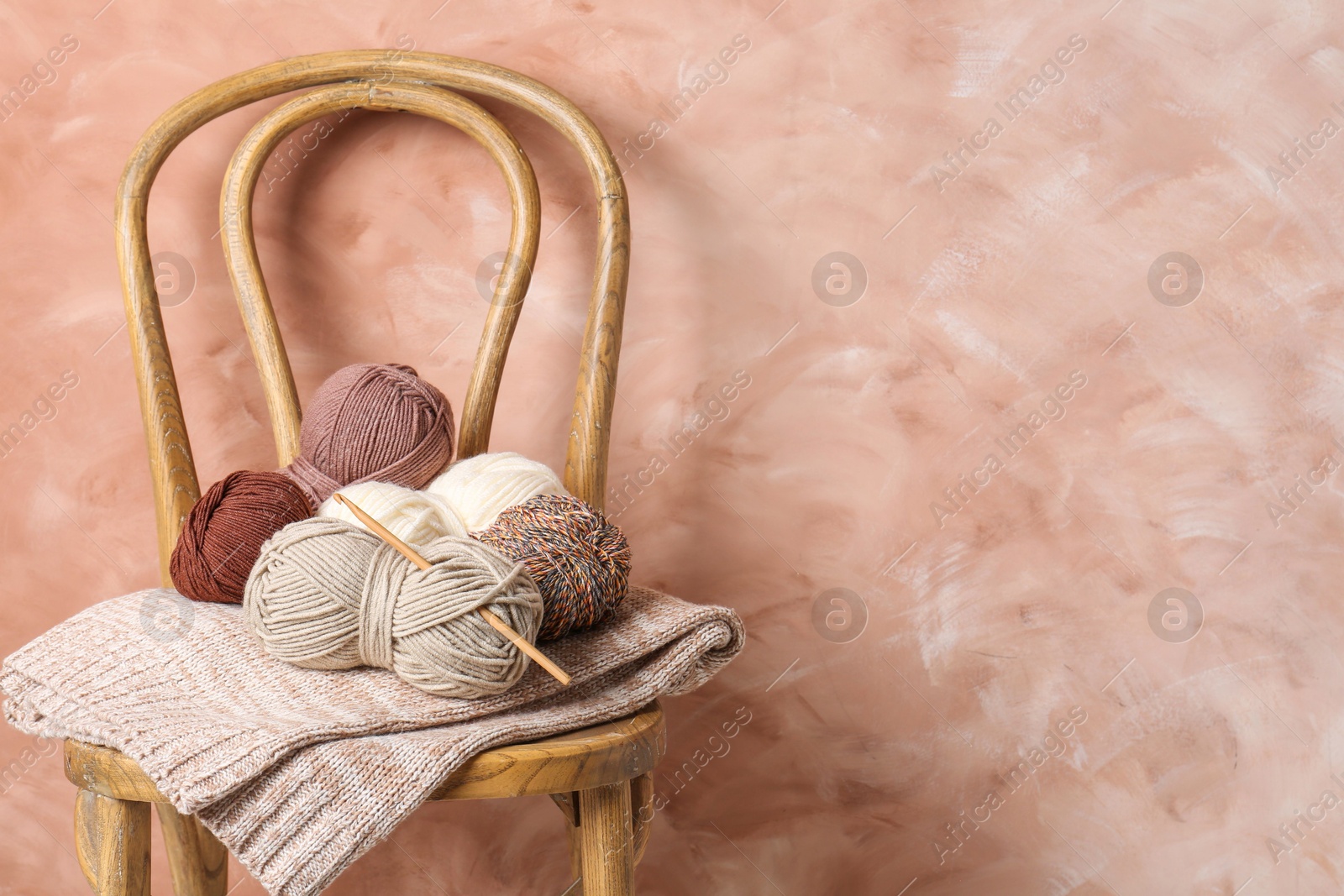 Photo of Different yarns, crochet hook and project on chair near beige wall. Space for text