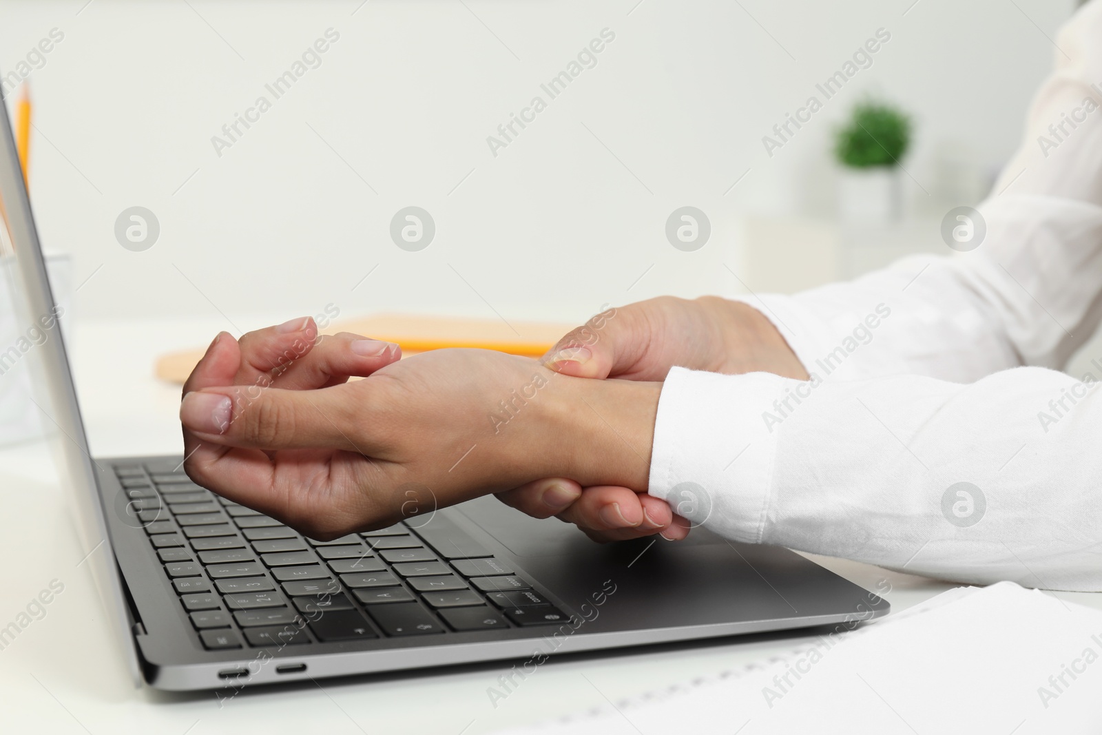 Photo of Carpal tunnel syndrome. Woman suffering from pain in wrist at desk indoors, closeup