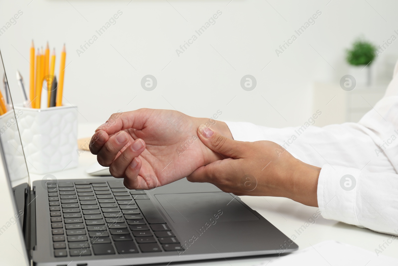 Photo of Carpal tunnel syndrome. Woman suffering from pain in wrist at desk indoors, closeup