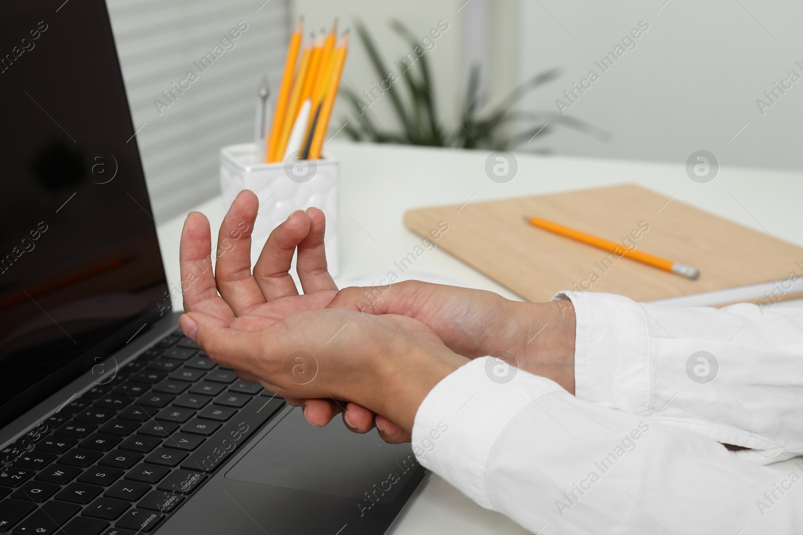 Photo of Carpal tunnel syndrome. Woman suffering from pain in wrist at desk indoors, closeup