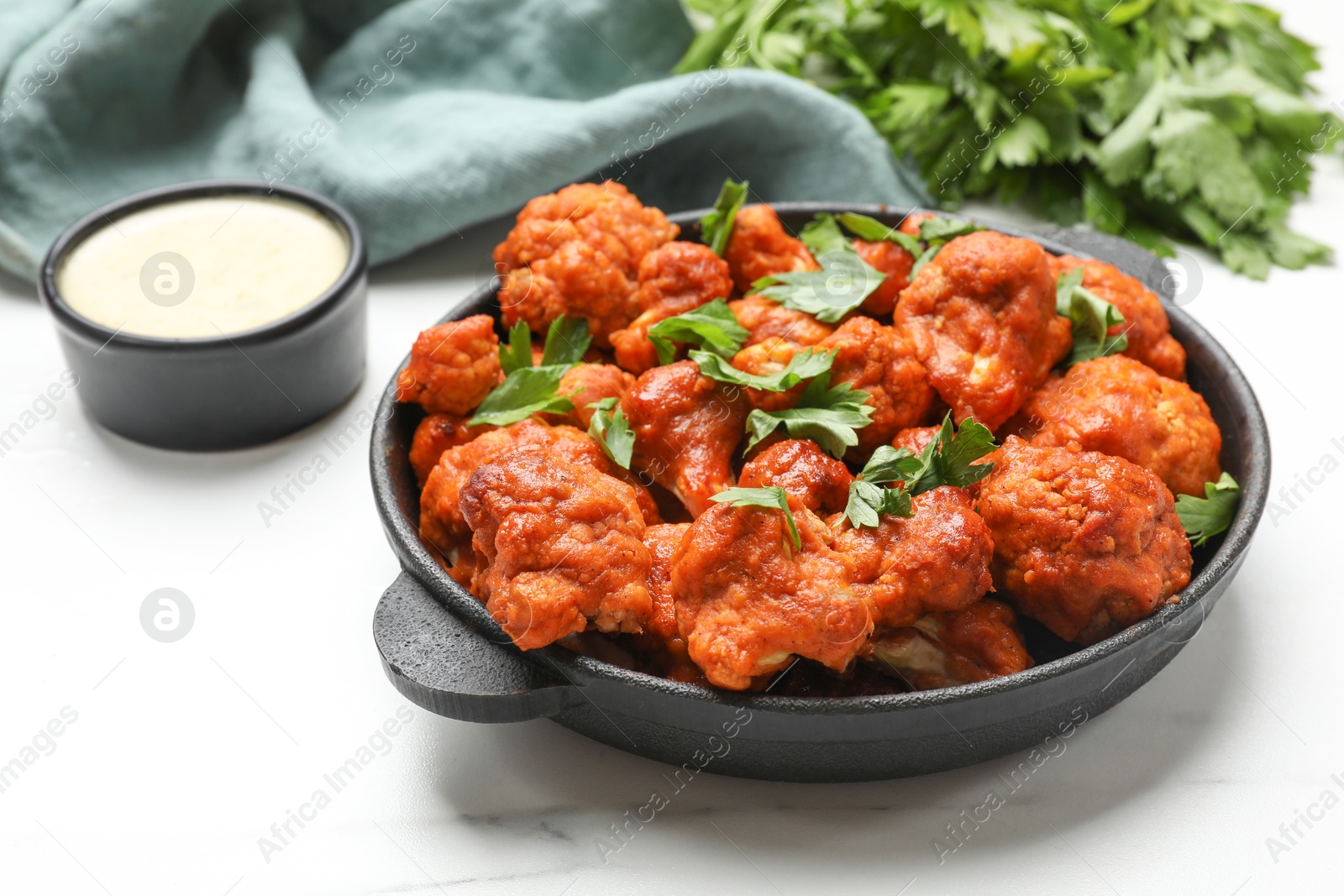 Photo of Baked cauliflower buffalo wings in baking dish, parsley and sauce on white marble table, closeup