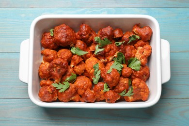 Photo of Baked cauliflower buffalo wings with parsley in baking dish on light blue wooden table, top view