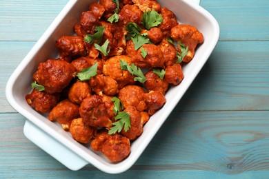 Photo of Baked cauliflower buffalo wings with parsley in baking dish on light blue wooden table, top view