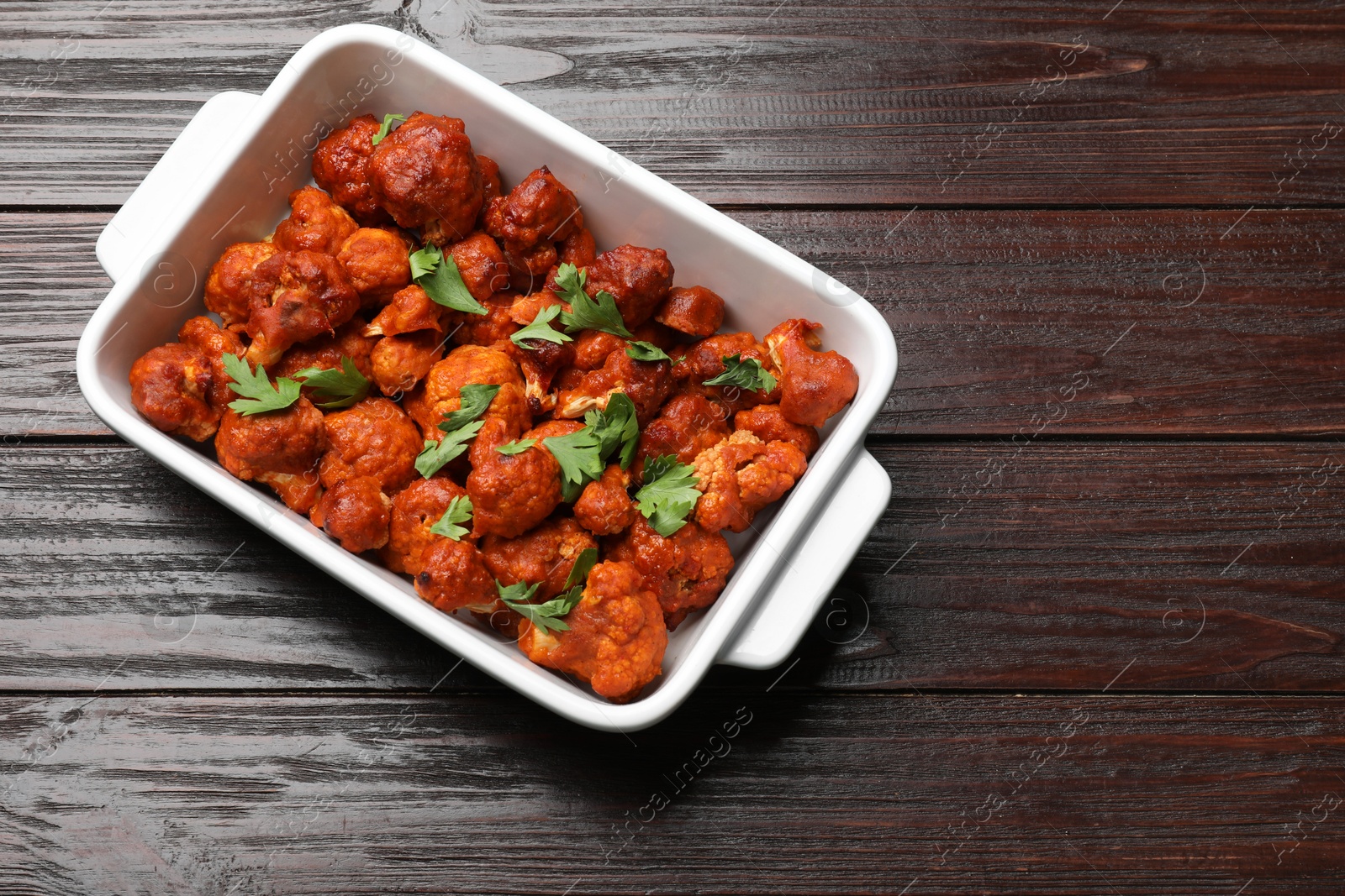 Photo of Baked cauliflower buffalo wings with parsley in baking dish on wooden table, top view. Space for text