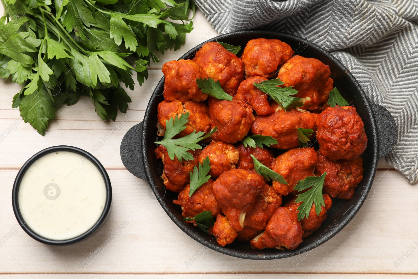 Photo of Baked cauliflower buffalo wings in baking dish, sauce and parsley on wooden table, top view