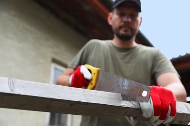 Man sawing wooden plank in backyard, selective focus