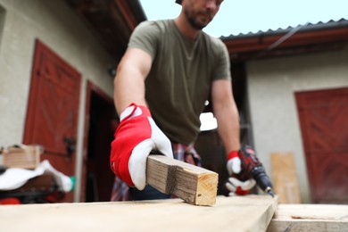 Photo of Man with wooden plank and electric screwdriver outdoors, closeup