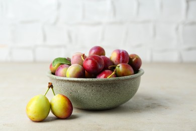 Photo of Tasty ripe plums in bowl on grey textured table