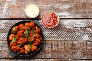 Photo of Baked cauliflower buffalo wings with parsley served on wooden table, flat lay. Space for text