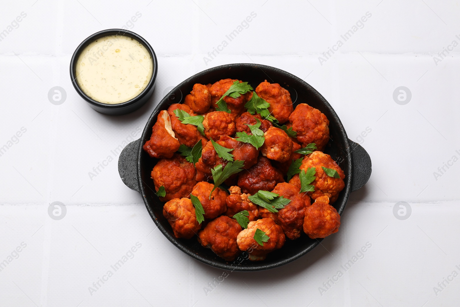 Photo of Baked cauliflower buffalo wings with parsley served on white tiled table, flat lay