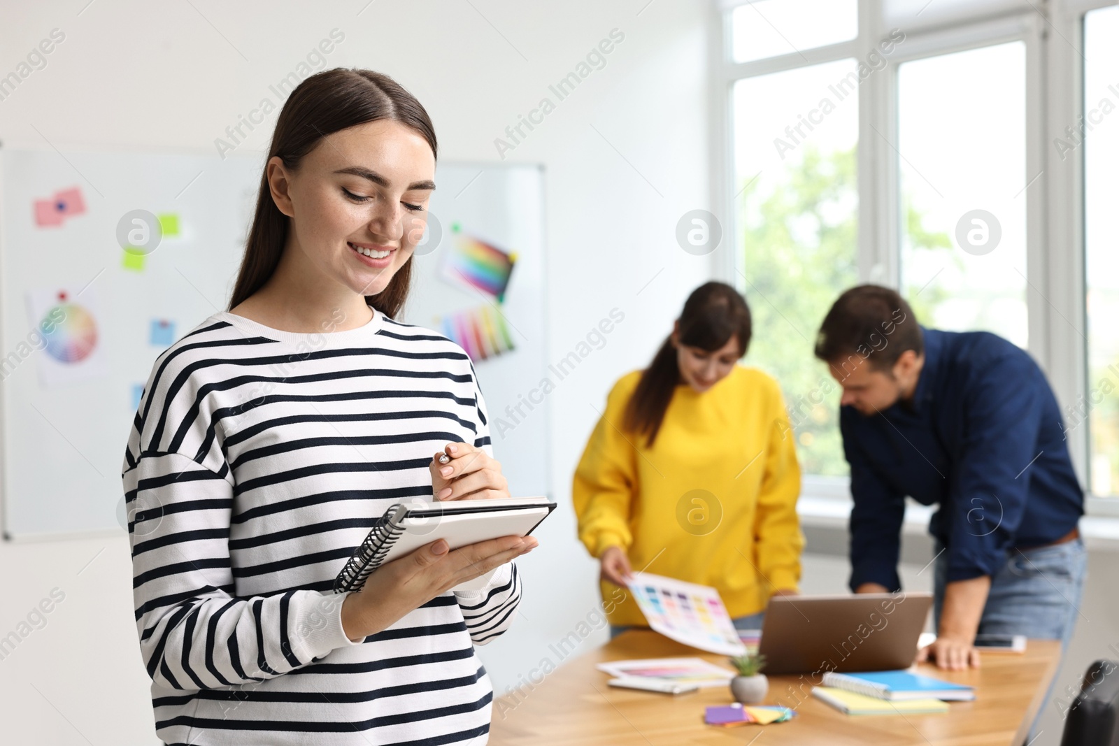 Photo of Portrait of happy young designer with notebook in office