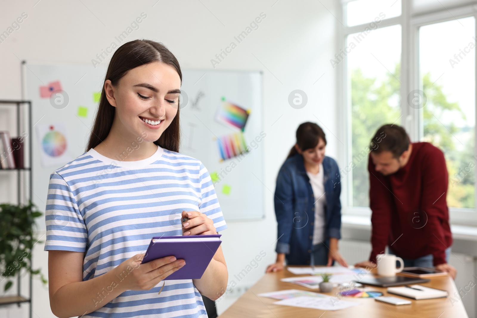 Photo of Portrait of happy young designer with notebook in office