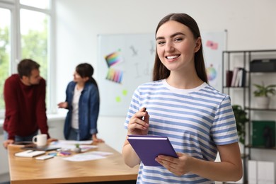 Photo of Portrait of happy young designer with notebook in office