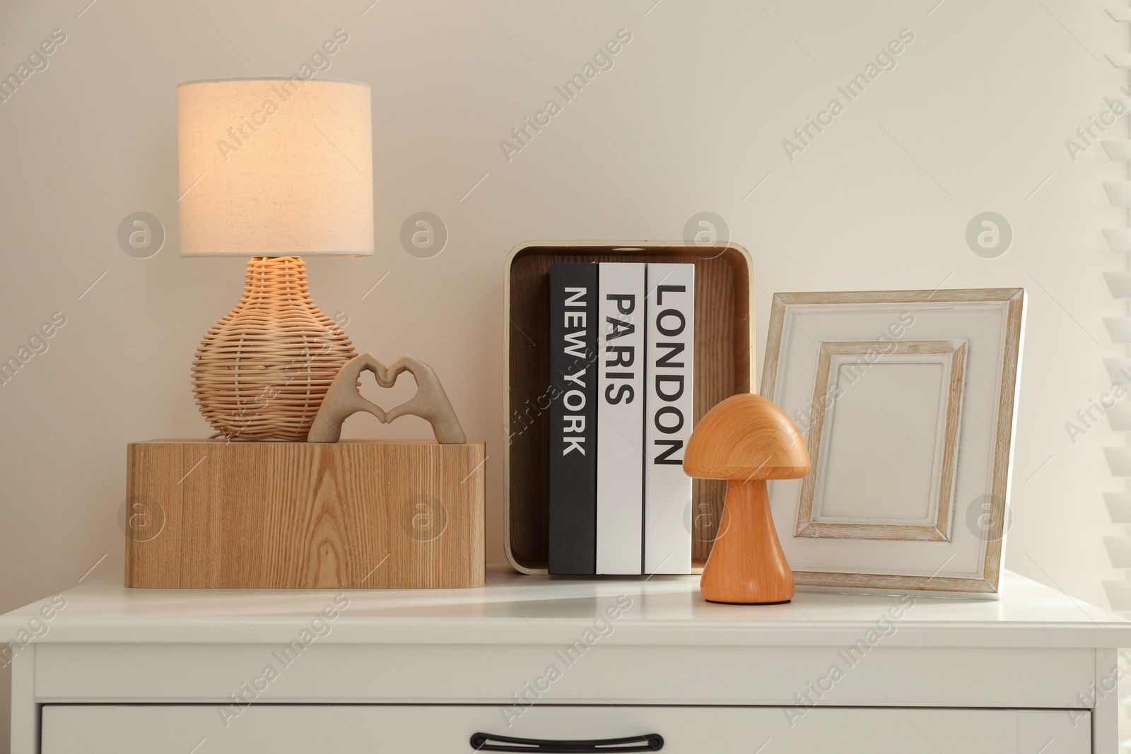 Photo of Beautiful decorative elements, books and lamp on chest of drawers