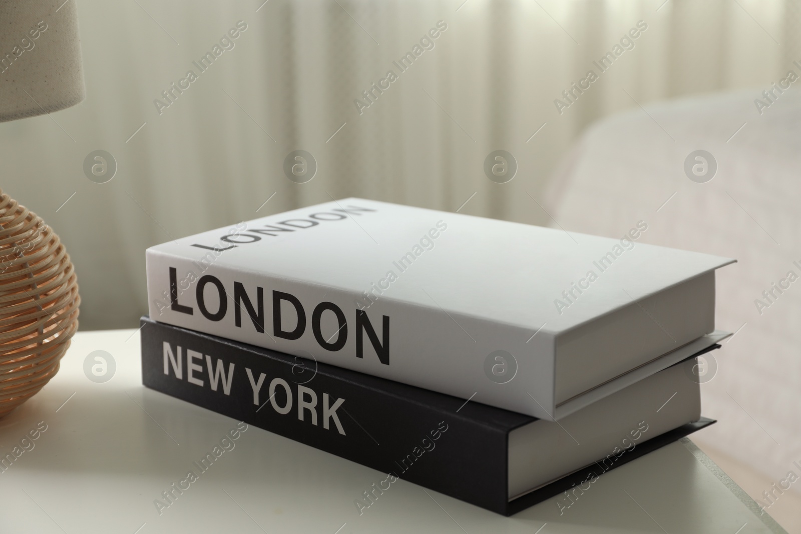 Photo of Books and lamp on nightstand near window indoors