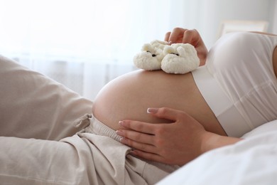 Photo of Young pregnant woman with baby shoes lying on bed at home, closeup