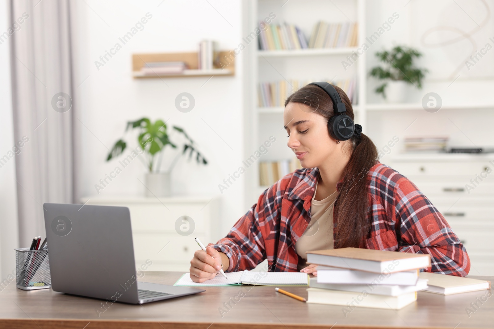 Photo of Student in headphones studying at wooden table indoors