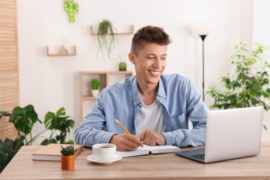 Photo of Student taking notes while studying at wooden table indoors