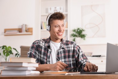 Photo of Student in headphones studying with laptop at table indoors