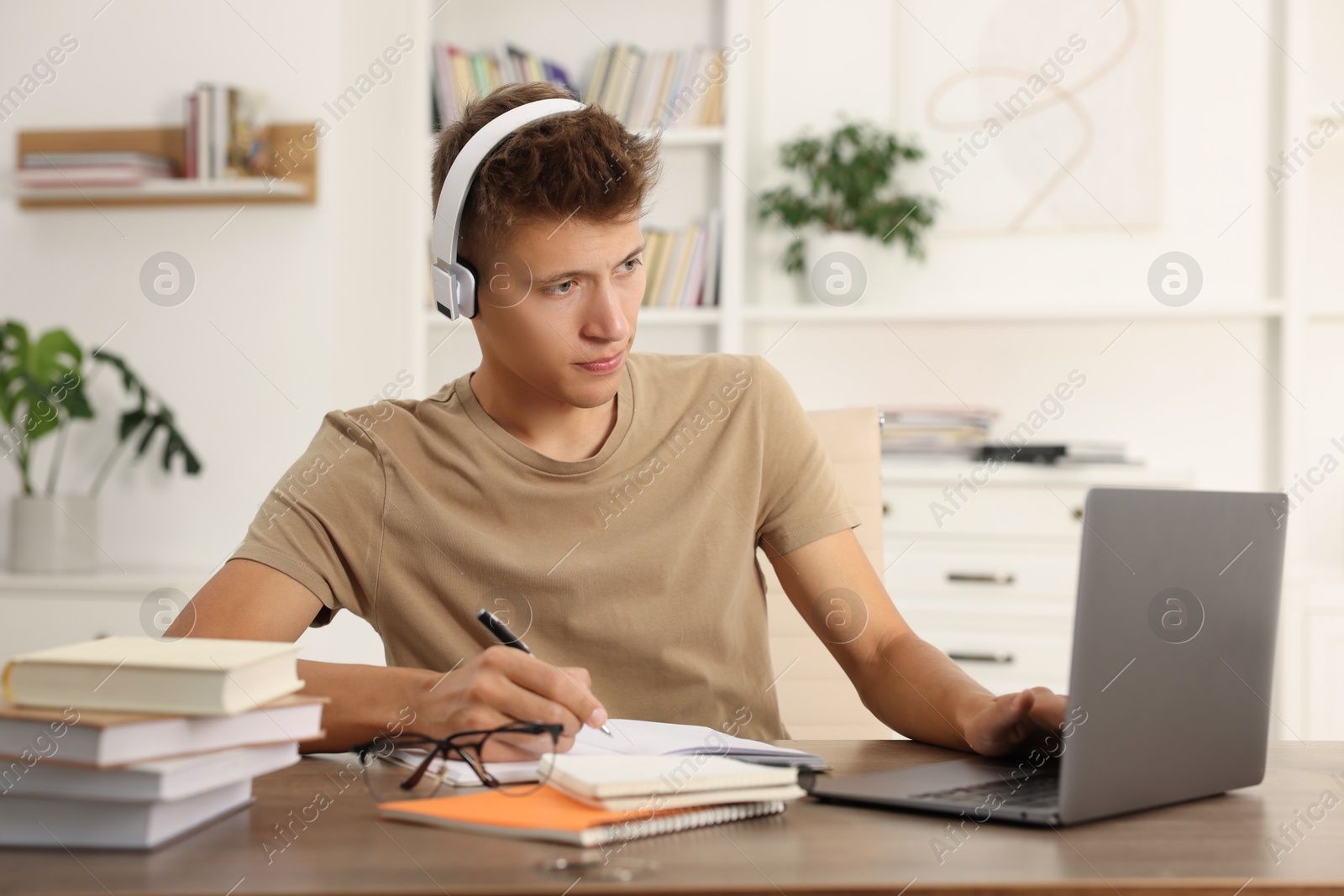 Photo of Student in headphones studying with laptop at table indoors