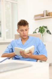 Photo of Medical student with book studying at table indoors