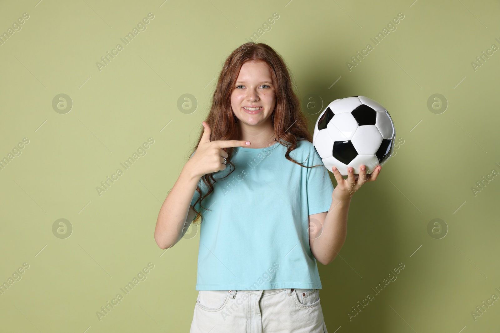 Photo of Smiling teenage girl pointing at soccer ball on green background