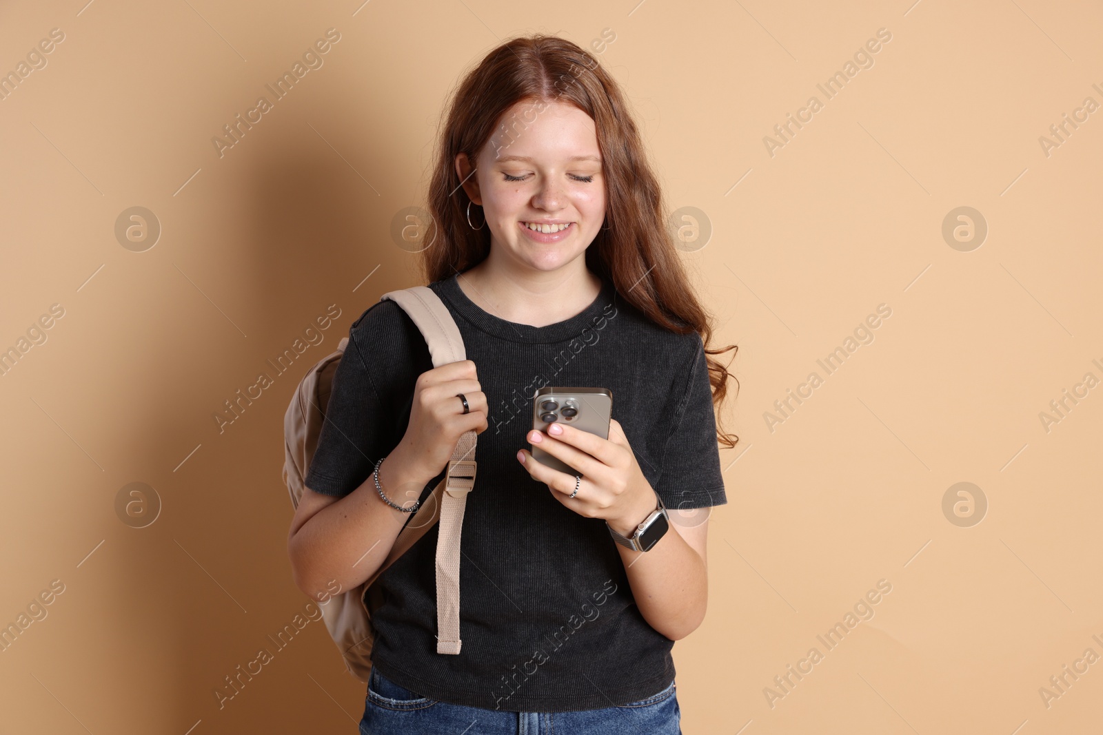 Photo of Smiling teenage girl with smartphone on beige background