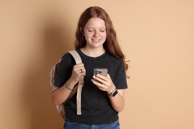 Smiling teenage girl with smartphone on beige background