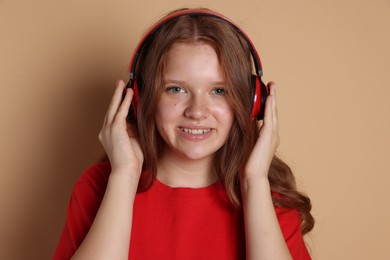 Smiling teenage girl in headphones listening to music on beige background