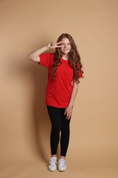 Photo of Smiling teenage girl showing peace sign on beige background