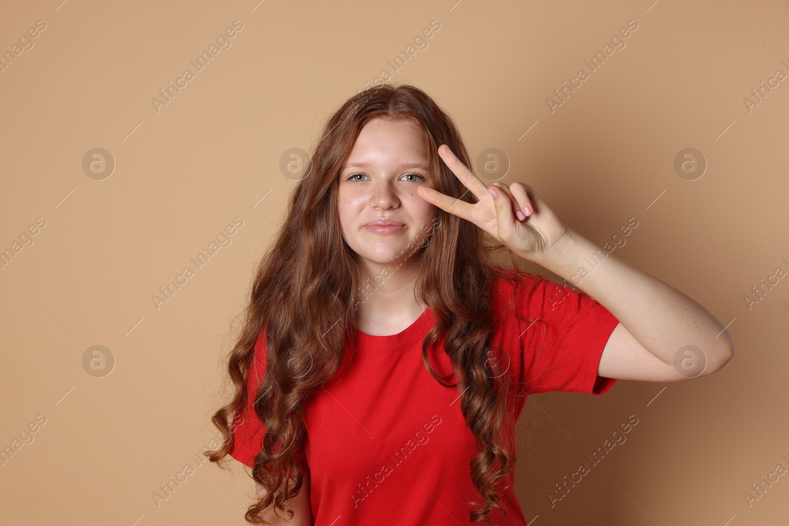 Photo of Cute teenage girl showing peace sign on beige background