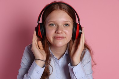 Cute teenage girl in headphones listening to music on pink background