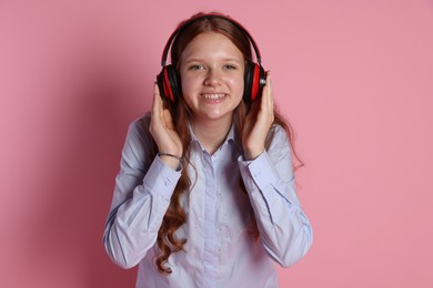 Smiling teenage girl in headphones listening to music on pink background