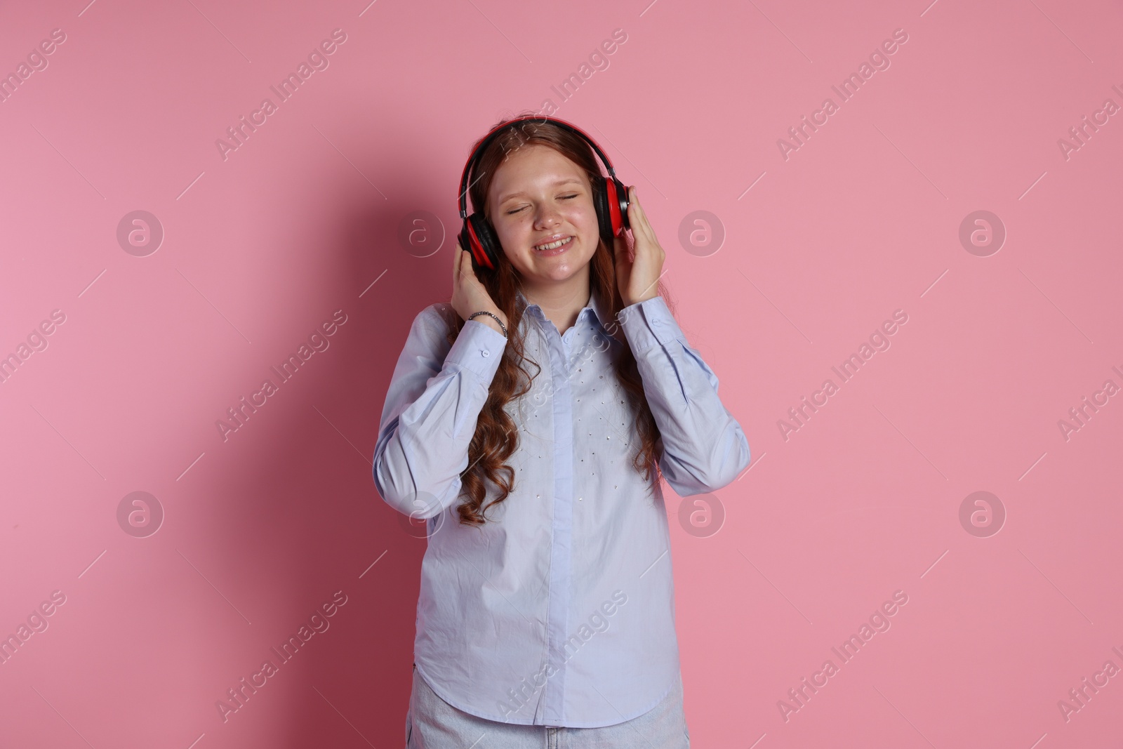 Photo of Smiling teenage girl in headphones listening to music on pink background