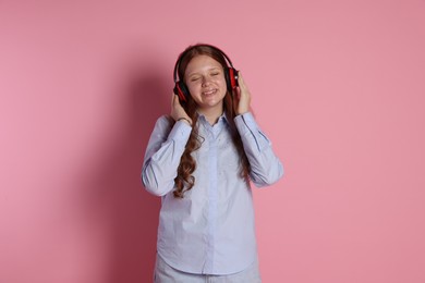 Smiling teenage girl in headphones listening to music on pink background