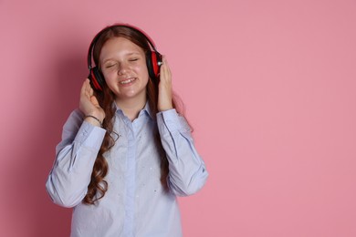 Smiling teenage girl in headphones listening to music on pink background. Space for text