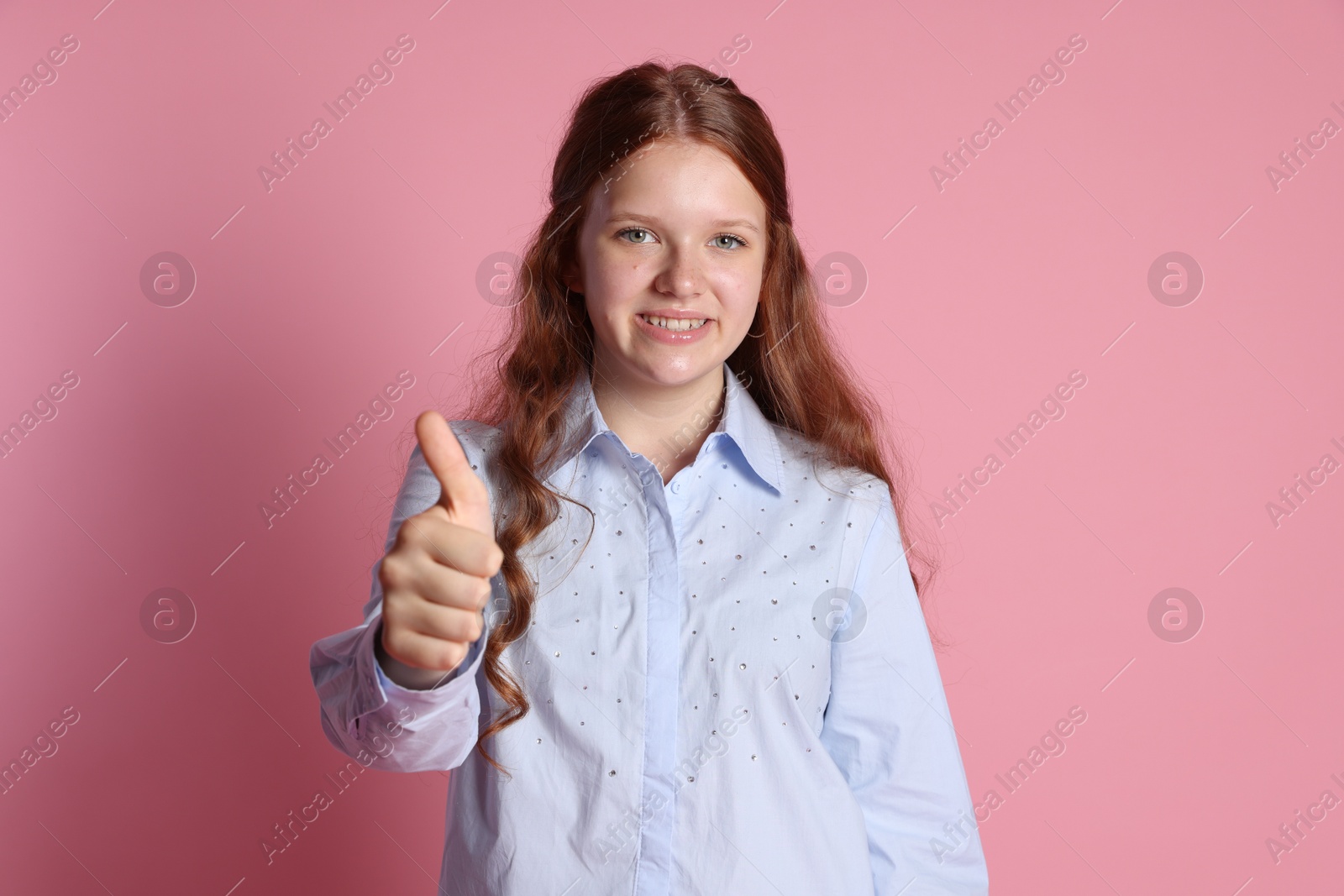 Photo of Happy teenage girl showing thumbs up on pink background