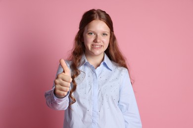 Happy teenage girl showing thumbs up on pink background