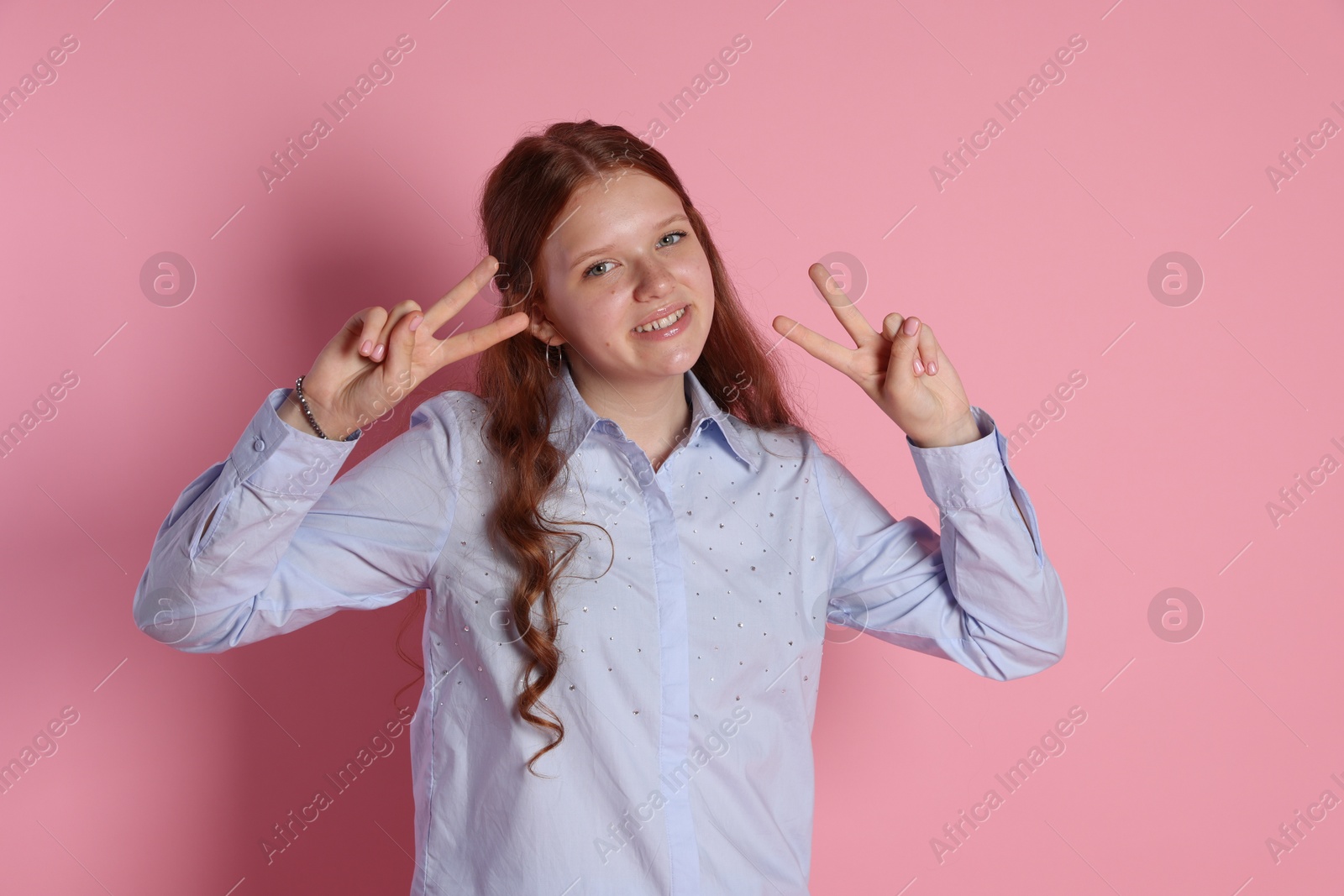 Photo of Happy teenage girl showing peace signs on pink background