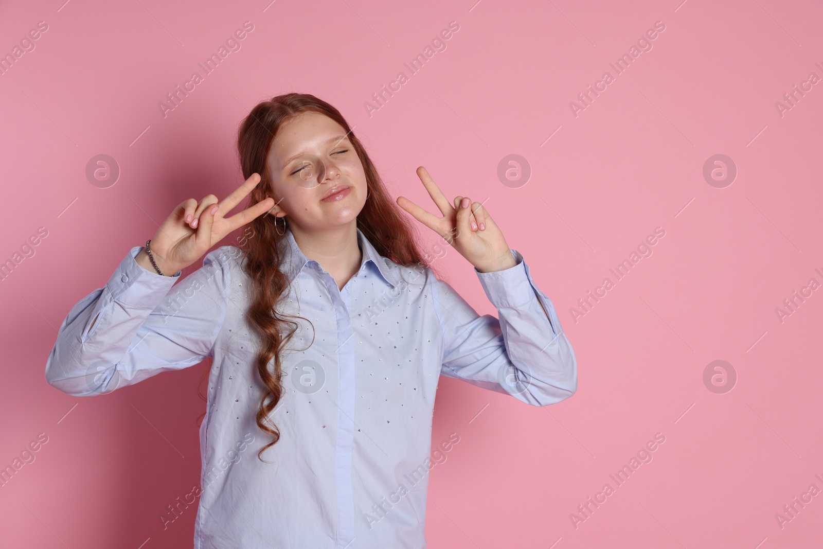 Photo of Cute teenage girl showing peace signs on pink background. Space for text