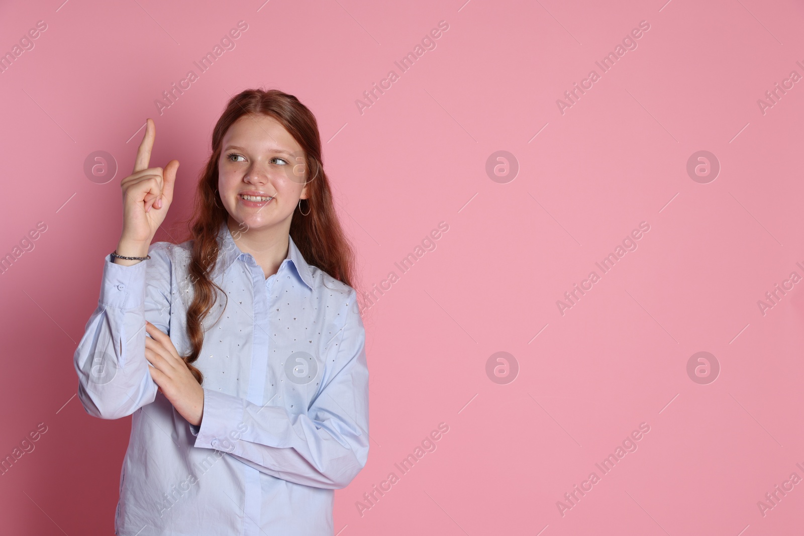 Photo of Happy teenage girl pointing upwards on pink background. Space for text