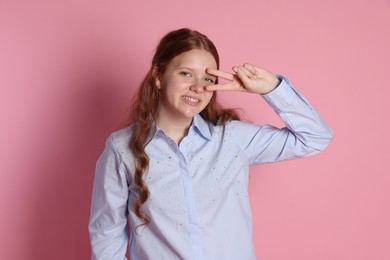 Happy teenage girl showing peace sign on pink background