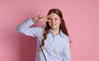 Photo of Happy teenage girl showing peace sign on pink background