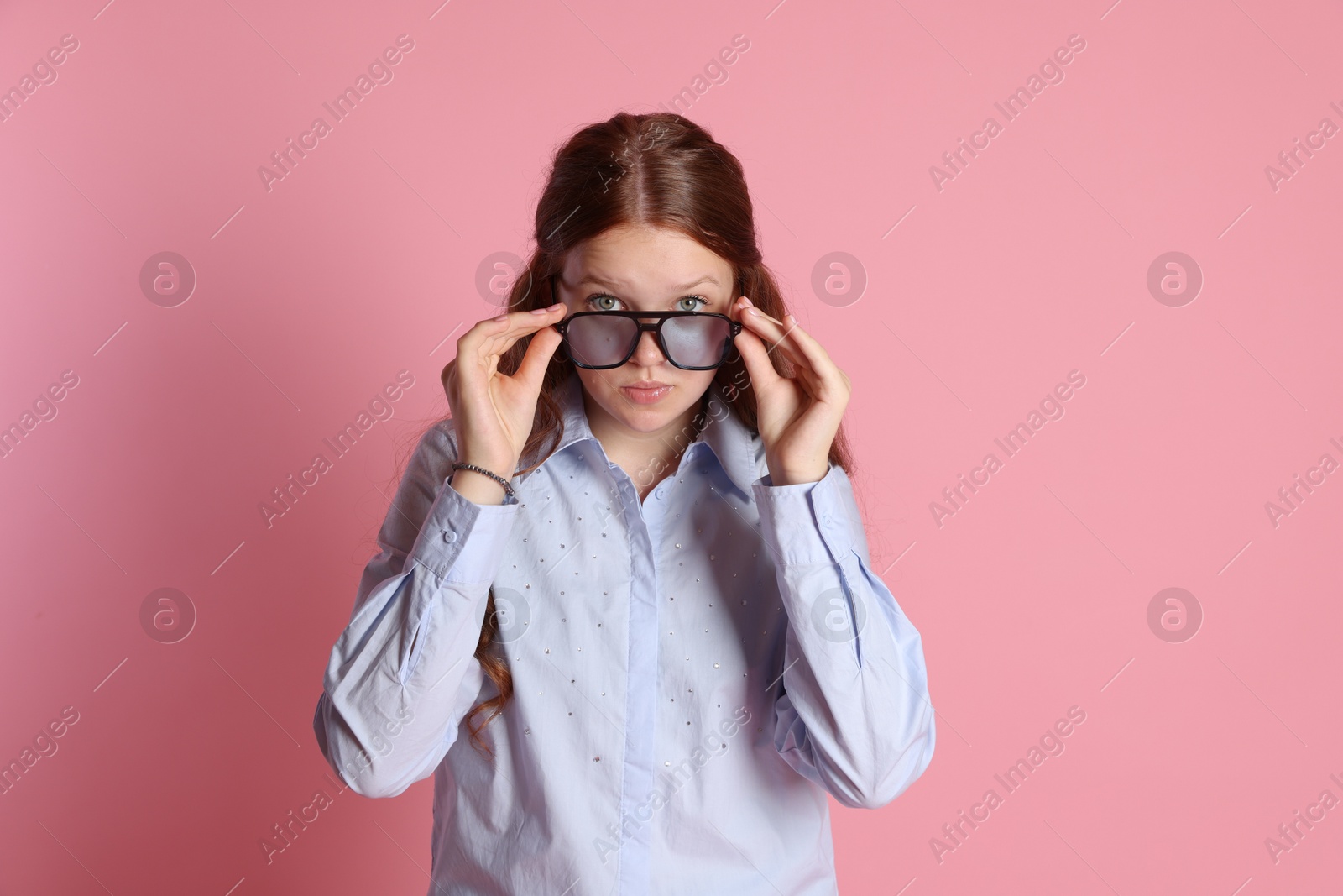 Photo of Cute teenage girl in sunglasses posing on pink background