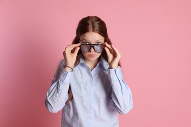 Cute teenage girl in sunglasses posing on pink background