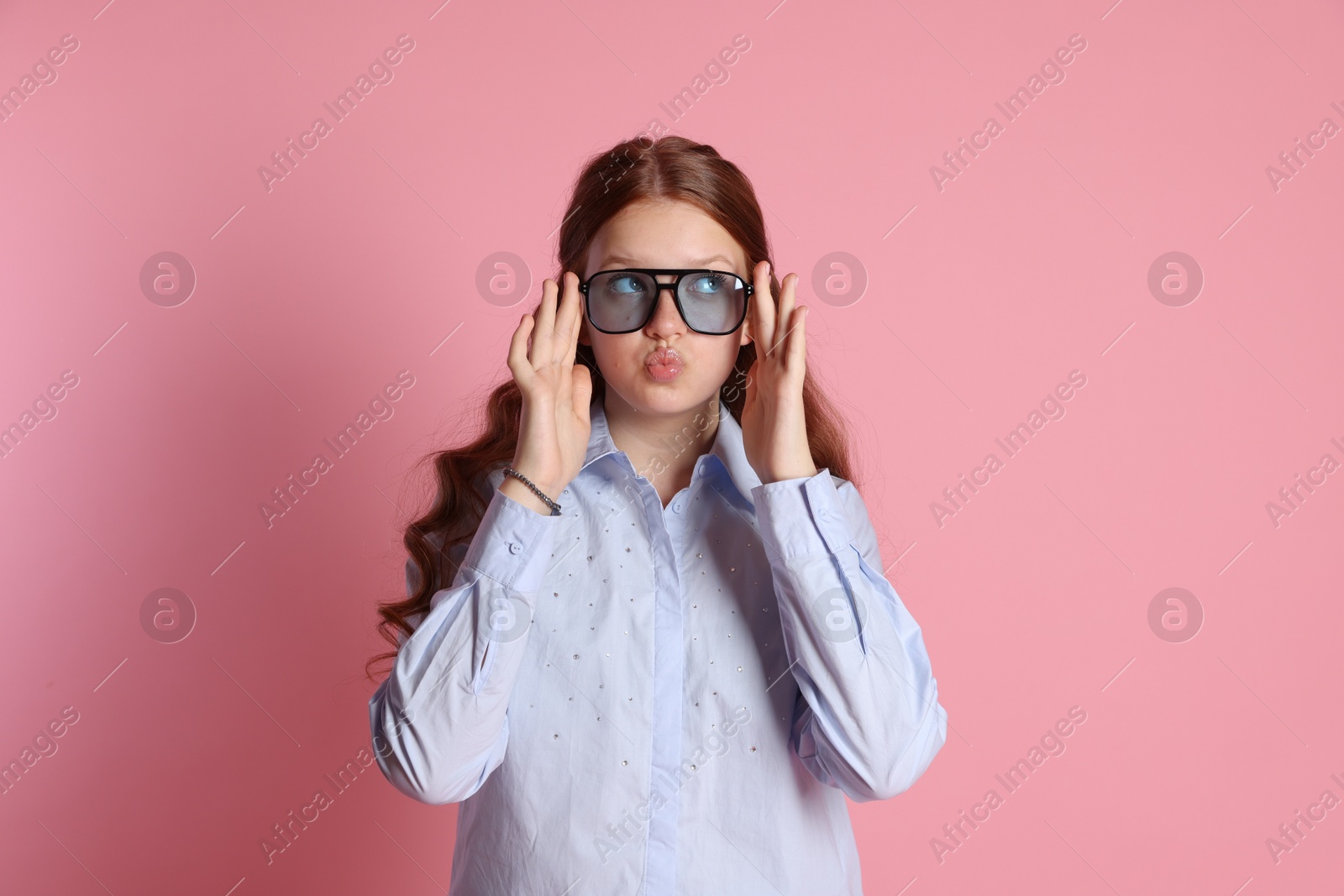 Photo of Cute teenage girl in sunglasses posing on pink background