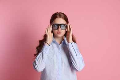 Cute teenage girl in sunglasses posing on pink background